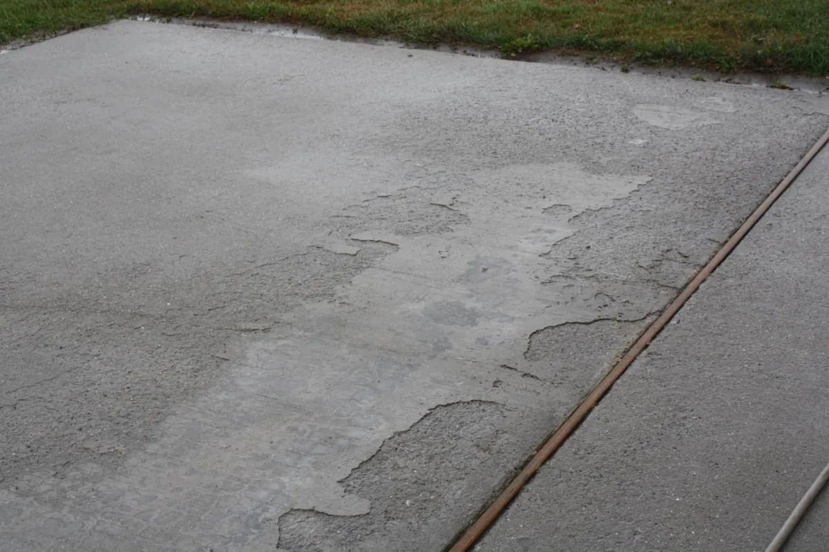 Concrete driveway with the top layer flaked away in patches